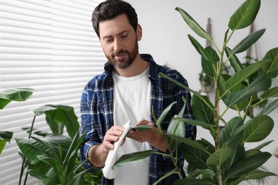 Man wiping leaves of beautiful potted houseplants with cloth indoors