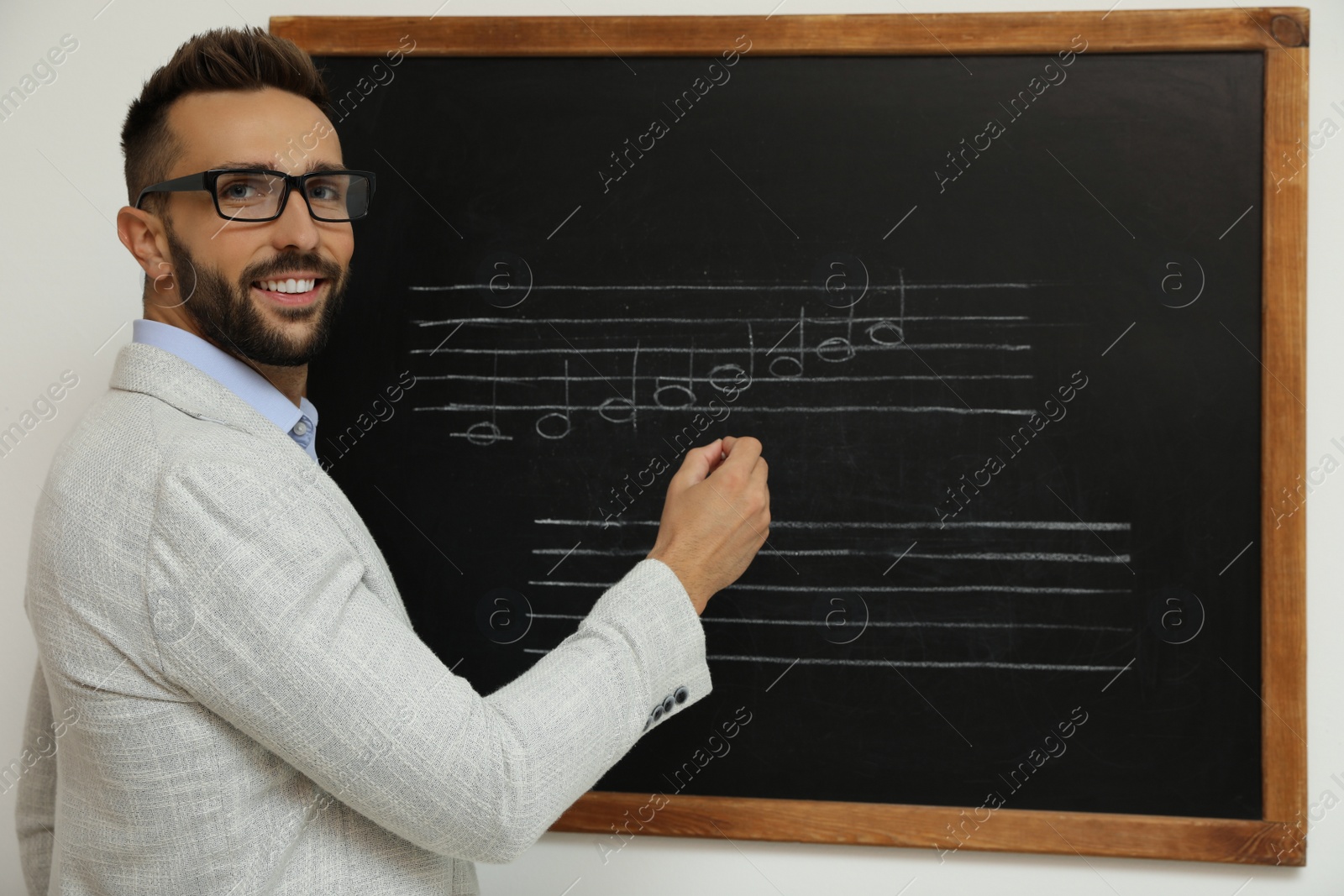 Photo of Teacher writing music notes with chalk on blackboard in classroom