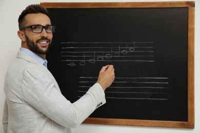 Teacher writing music notes with chalk on blackboard in classroom