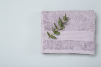 Photo of Violet terry towel and eucalyptus branch on light grey background, top view. Space for text
