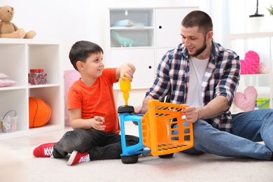 Photo of Man and his child as repairman playing with toy cart at home