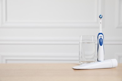 Photo of Electric toothbrush, glass of water and toothpaste on wooden table. Space for text