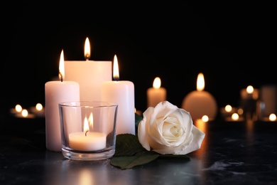 White rose and burning candles on table in darkness. Funeral symbol