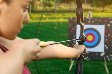 Photo of Woman with bow and arrow aiming at archery target in park, closeup