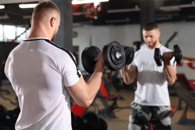 Photo of Man training with dumbbells near mirror in gym