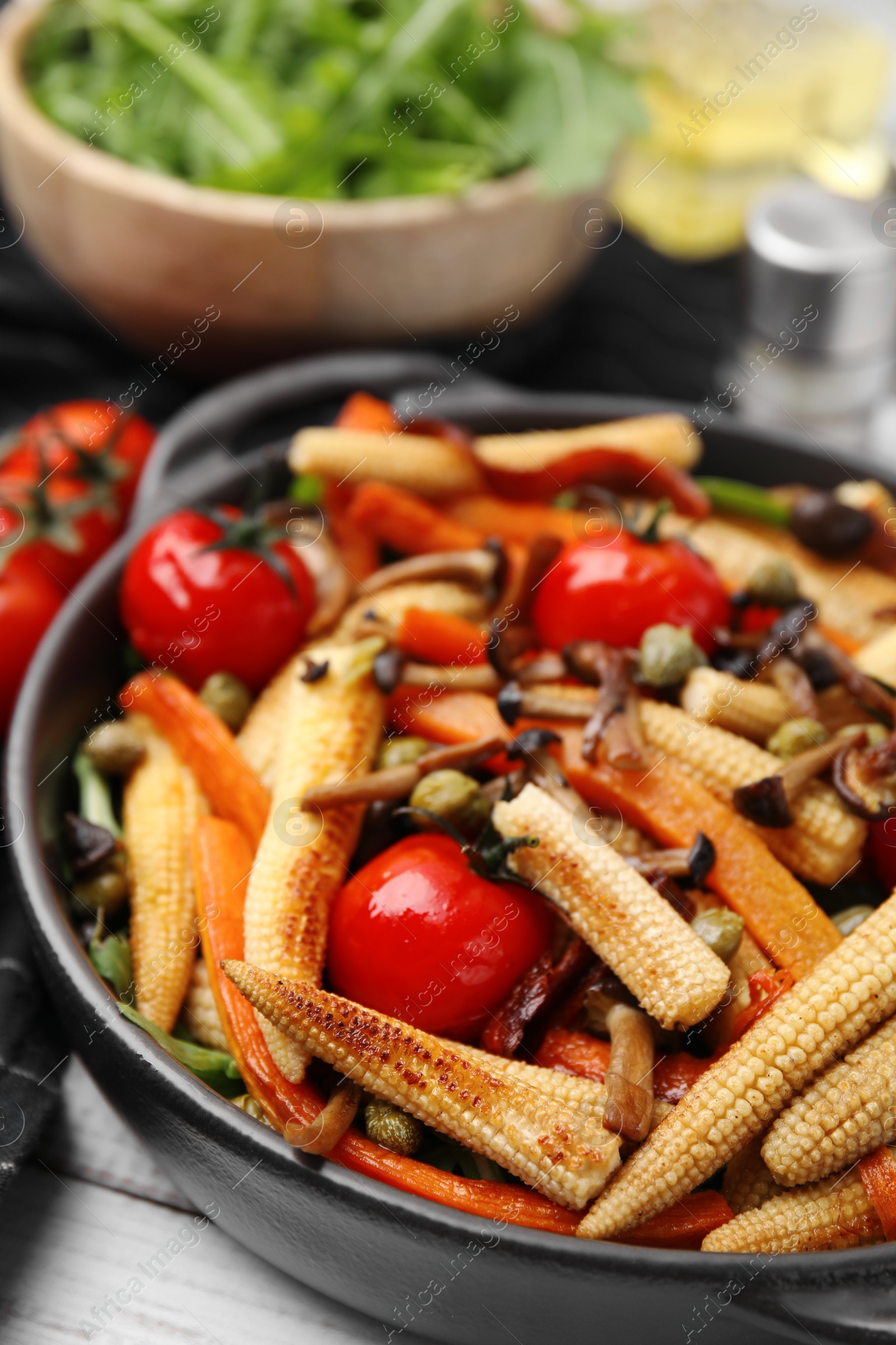 Photo of Tasty roasted baby corn with tomatoes, capers and mushrooms on white wooden table, closeup