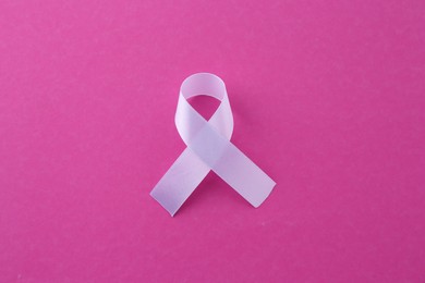 White awareness ribbon on pink background, top view