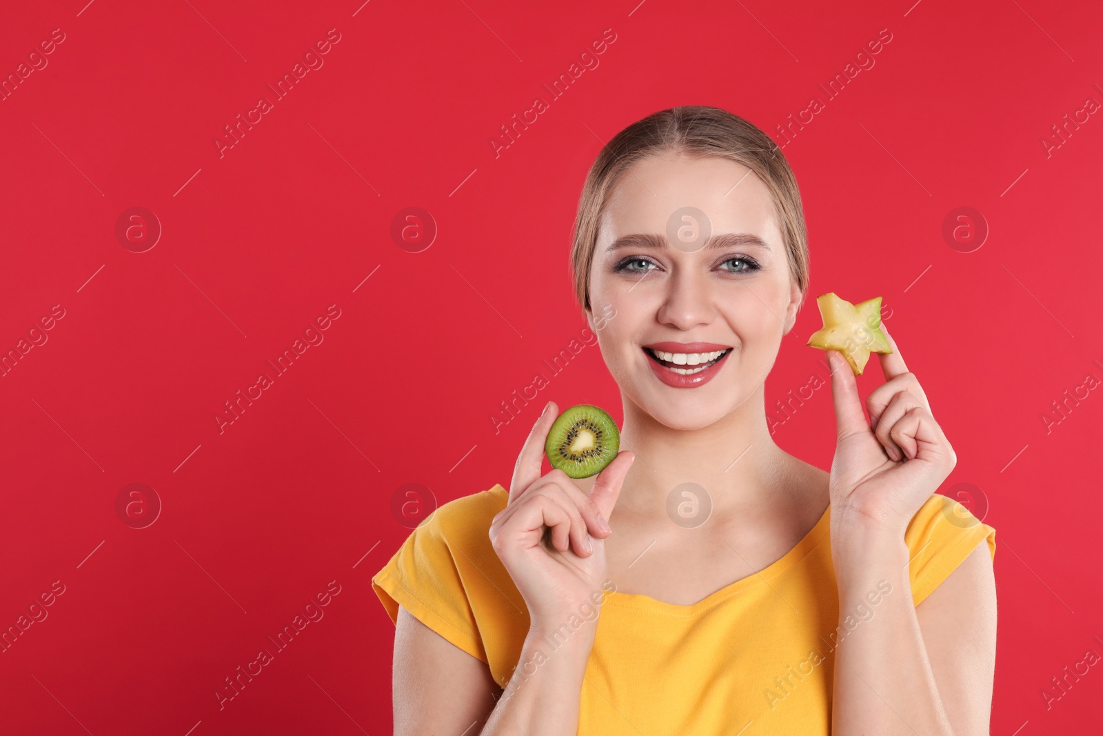 Photo of Young woman with cut kiwi and carambola on red background, space for text. Vitamin rich food