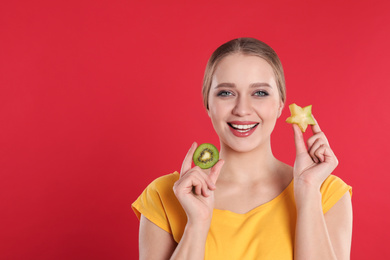 Photo of Young woman with cut kiwi and carambola on red background, space for text. Vitamin rich food