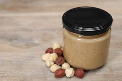 Tasty nut paste in jar and hazelnuts on wooden table, closeup. Space for text