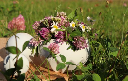 Photo of Ceramic mortar with pestle, different wildflowers and herbs on wooden board in meadow, closeup