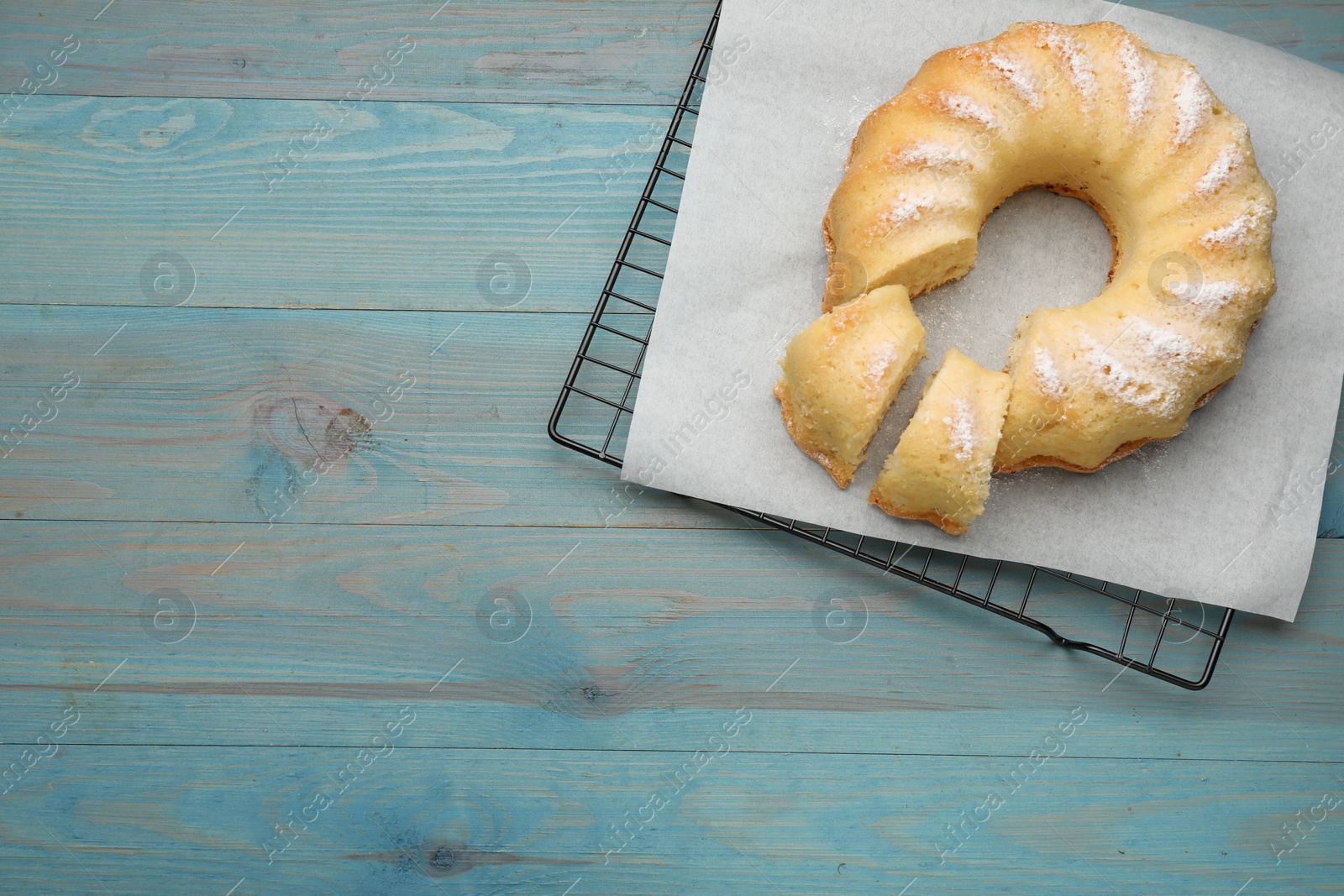 Photo of Delicious freshly baked sponge cake on light blue wooden table, top view. Space for text