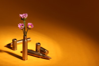 Photo of Bullet cartridge cases and beautiful chrysanthemum flowers on orange background, space for text