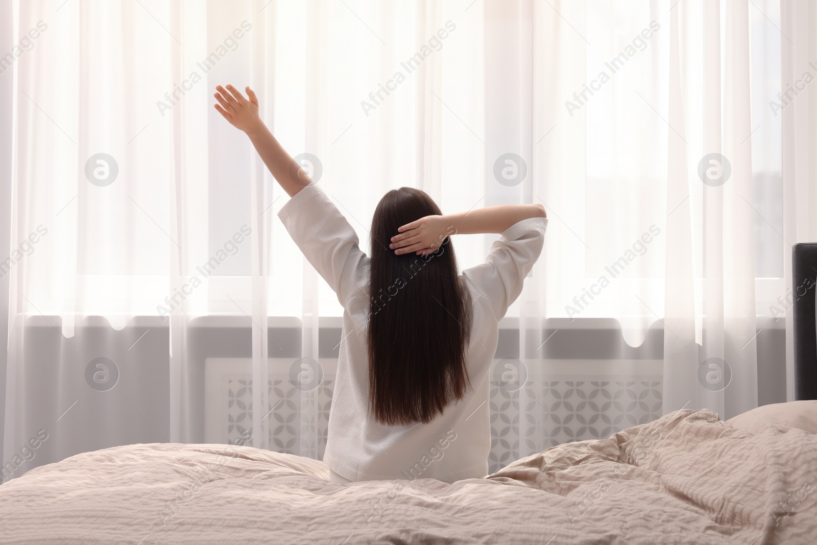 Photo of Woman stretching on bed at home, back view. Lazy morning