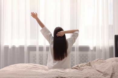 Woman stretching on bed at home, back view. Lazy morning