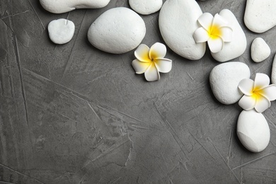 Zen stones and exotic flowers on dark background, top view with space for text