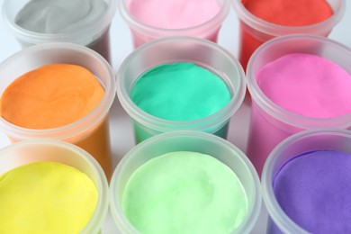 Photo of Plastic containers with colorful play dough on white background, closeup
