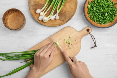 Photo of Woman cutting fresh green onion on table, top view