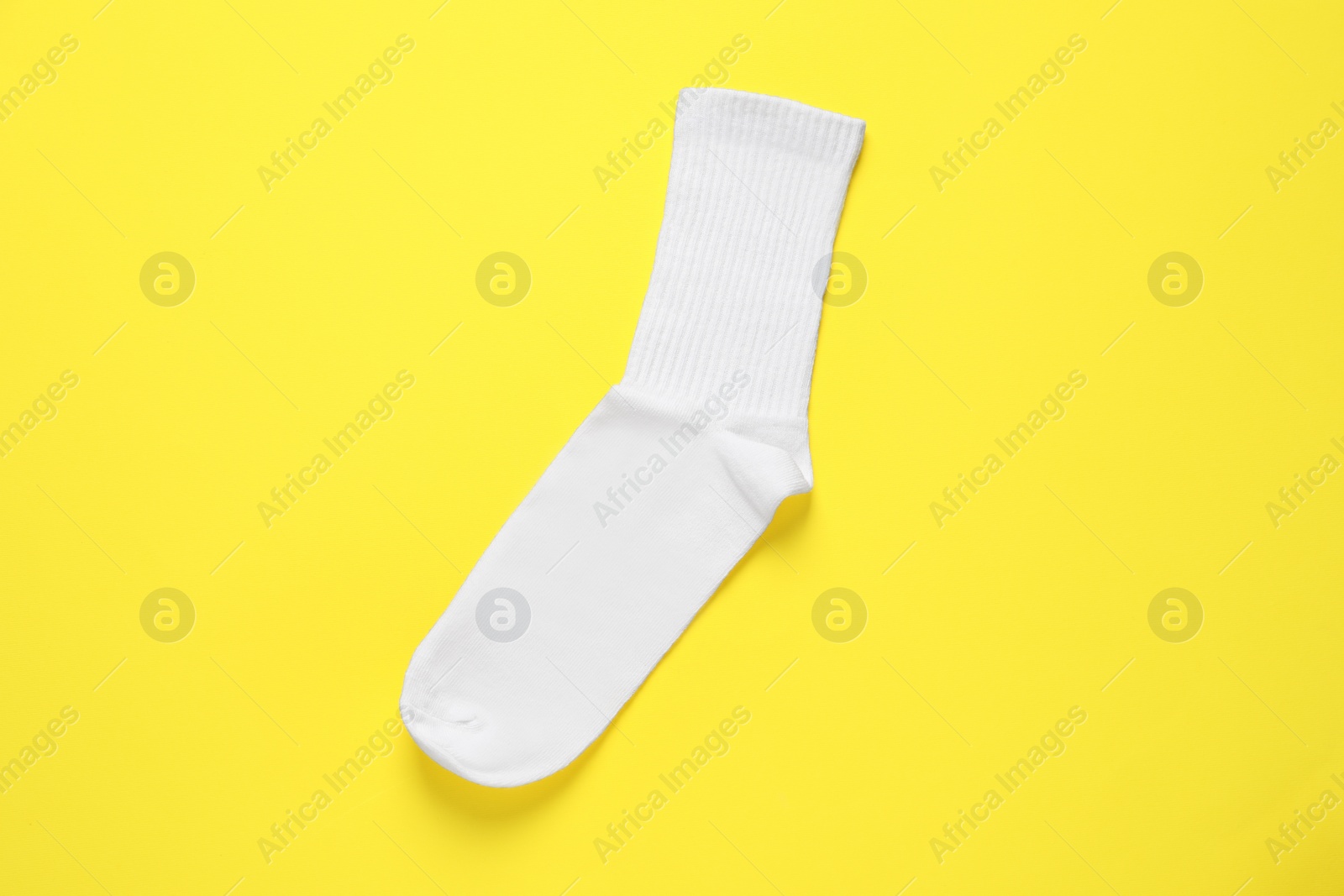 Photo of One white sock on yellow background, top view