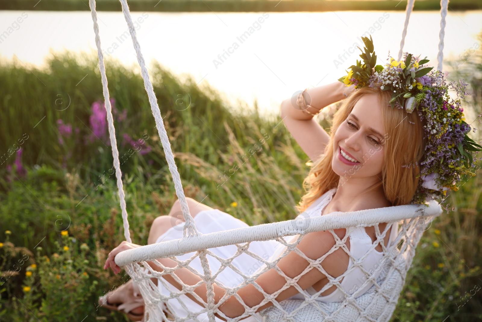 Photo of Young woman wearing wreath made of beautiful flowers on swing chair outdoors