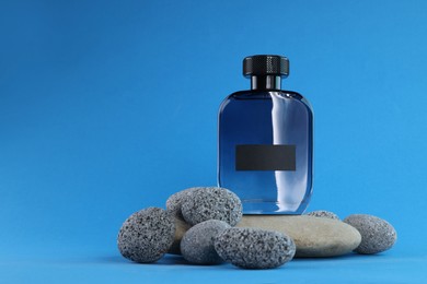 Photo of Stylish presentation of luxury men`s perfume on stones against light blue background. Space for text