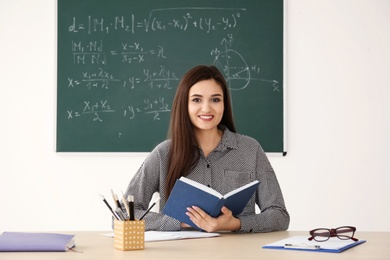 Photo of Young female teacher working at table in classroom