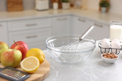 Metal whisk, bowl, grater and different products on gray marble table in kitchen