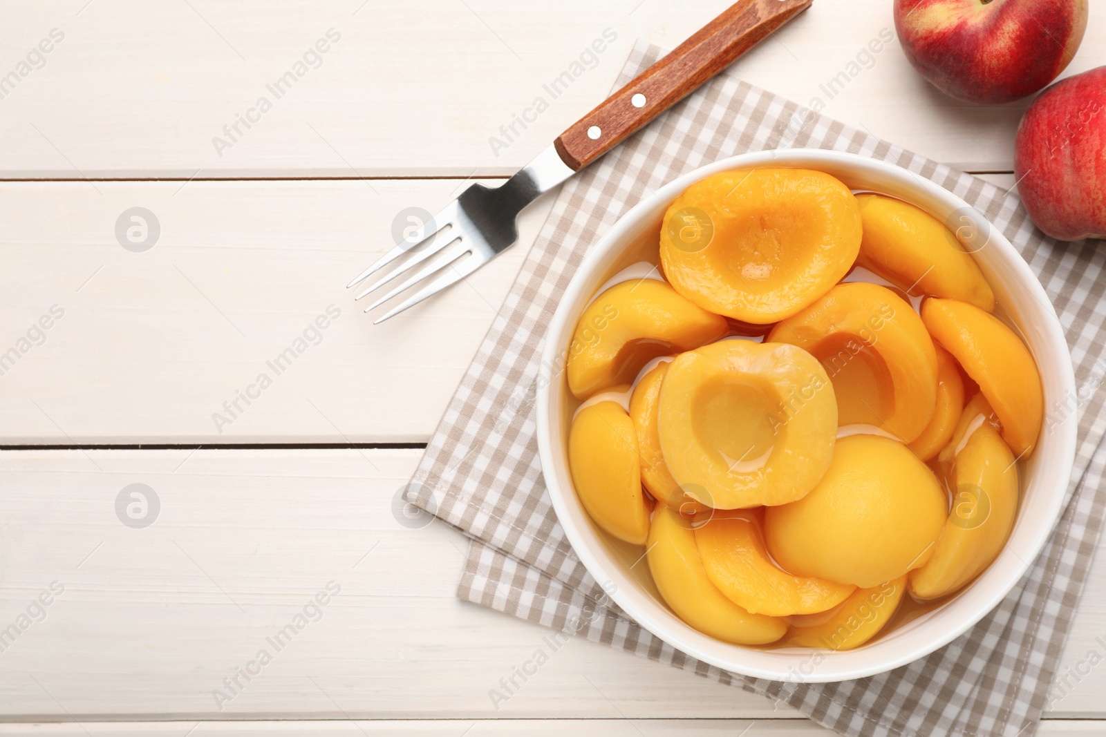 Photo of Canned peach halves and fork on white wooden table, flat lay. Space for text