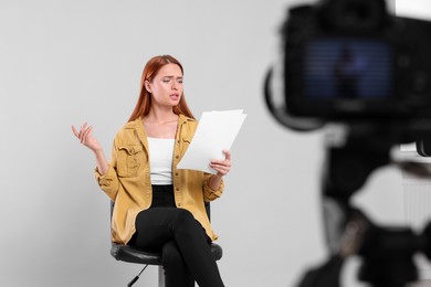Photo of Casting call. Young woman with script performing in front of camera against light grey background at studio