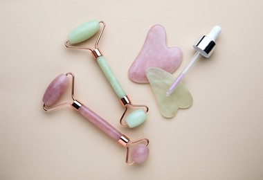 Gua sha tools, facial rollers and dropper on beige background, flat lay