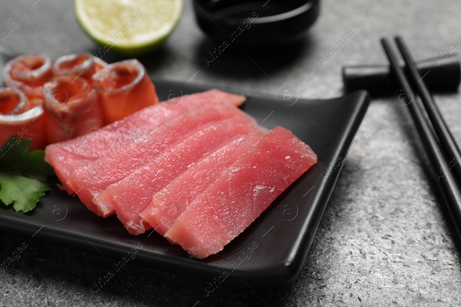 Photo of Sashimi set (raw tuna and salmon slices) with parsley on grey table, closeup