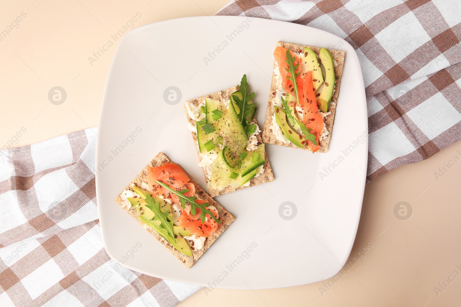 Photo of Fresh crunchy crispbreads with cream cheese, cucumber, green onion, salmon and arugula on beige table, flat lay