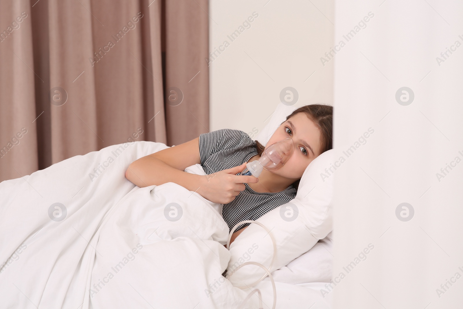 Photo of Cute girl using nebulizer for inhalation on bed at home