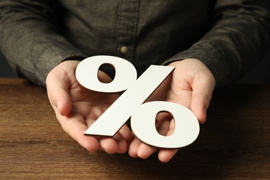 Photo of Man holding percent sign at wooden table, closeup