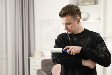 Photo of Pet shedding. Man with lint roller removing dog's hair from sweater at home. Space for text