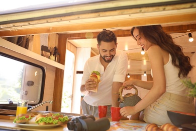 Photo of Happy young couple having breakfast in trailer, view from outside. Camping vacation