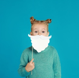 Cute little girl with Santa beard prop on light blue background. Christmas celebration