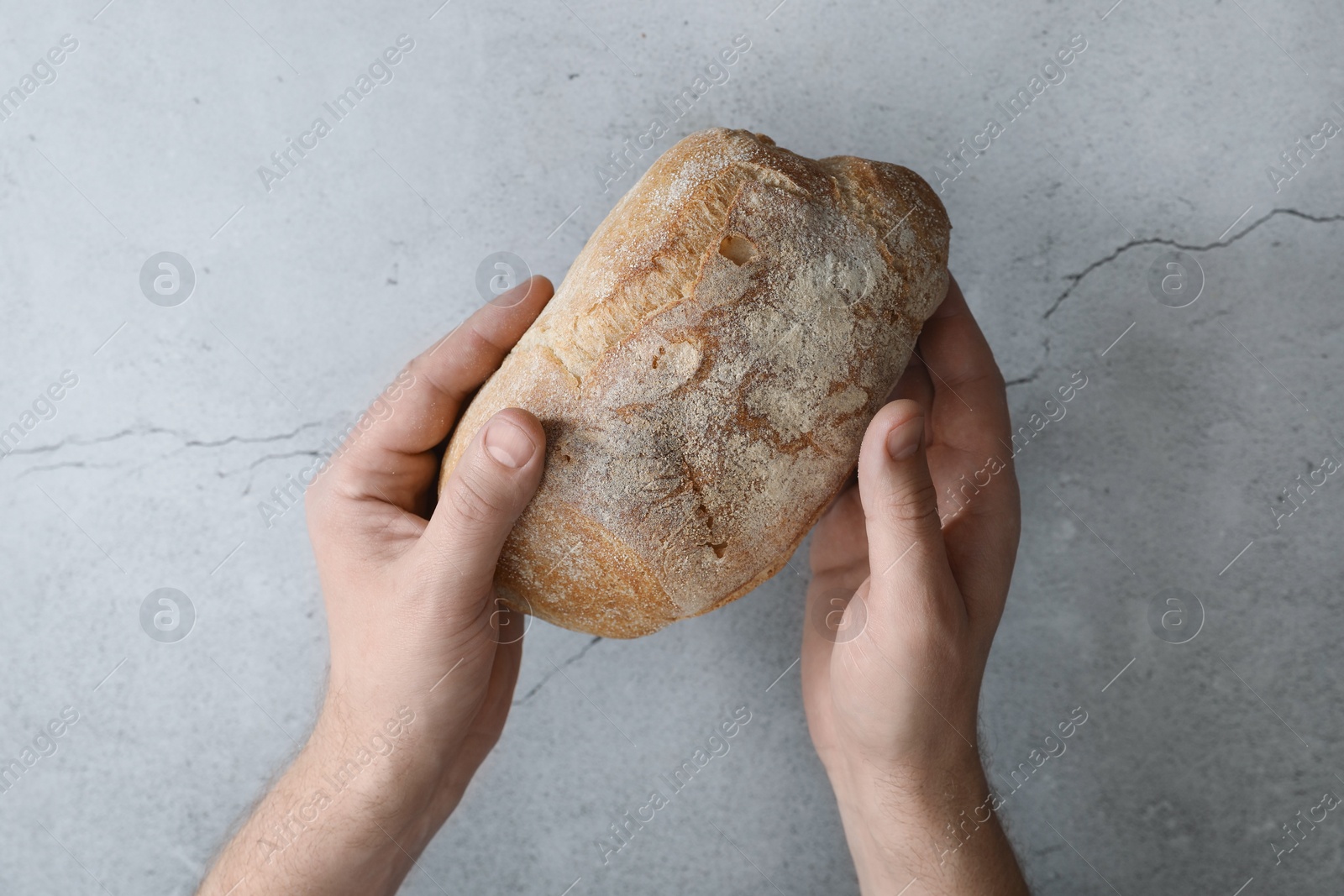 Photo of Man holding loaf of fresh bread at grey table, top view