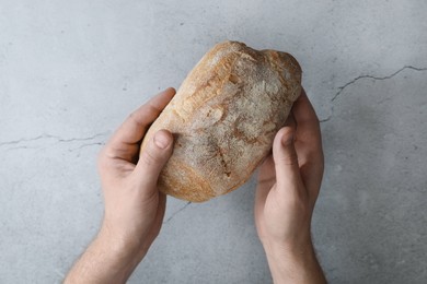 Photo of Man holding loaf of fresh bread at grey table, top view