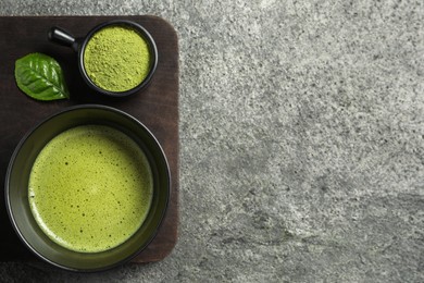 Photo of Cup of fresh matcha tea and green powder on grey table, top view. Space for text