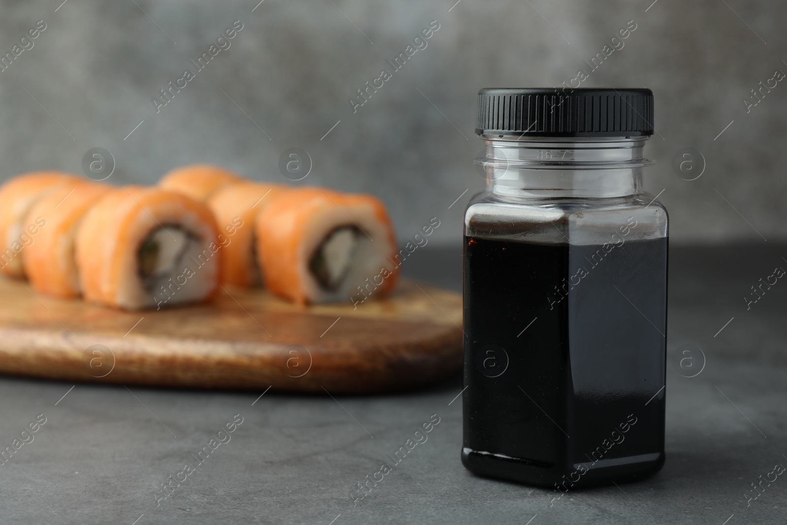 Photo of Bottle of tasty soy sauce and sushi rolls on grey table, space for text