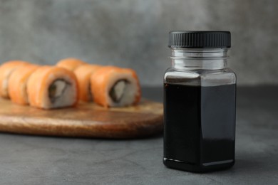 Bottle of tasty soy sauce and sushi rolls on grey table, space for text