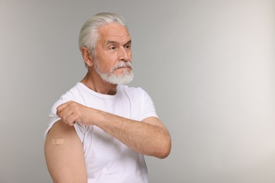 Senior man with adhesive bandage on his arm after vaccination against light grey background, space for text