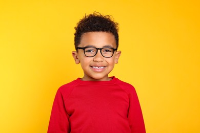 Photo of Portrait of cute African-American boy with glasses on yellow background