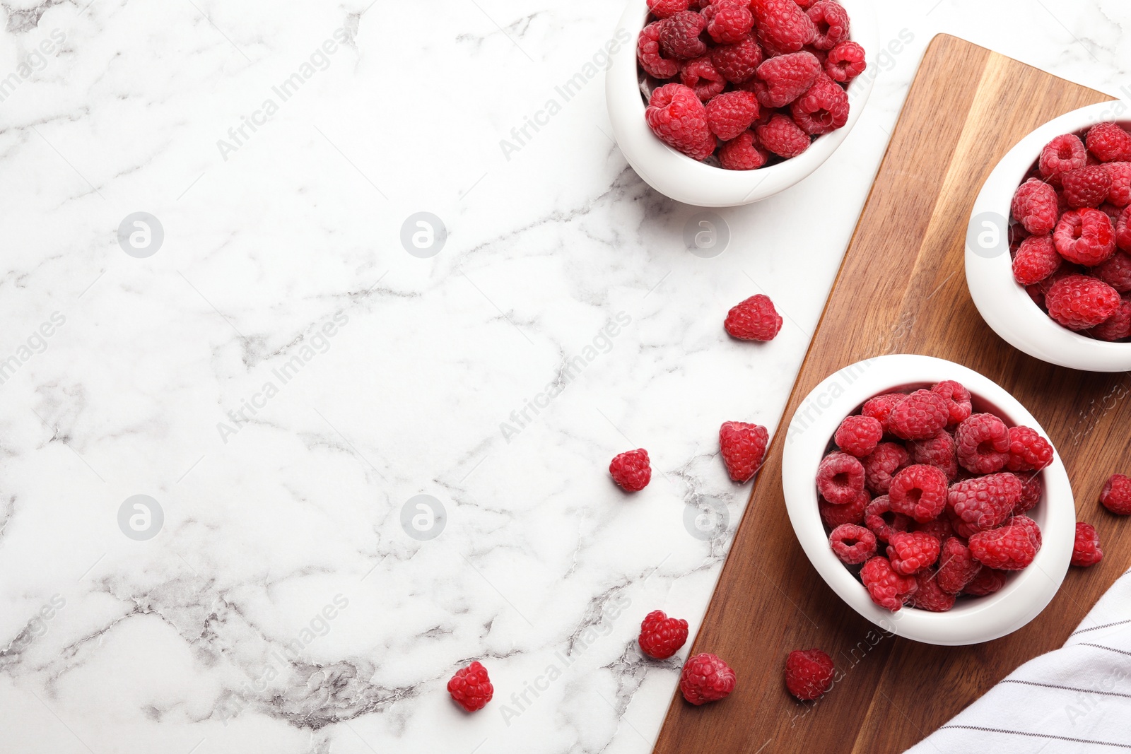 Photo of Bowls with delicious ripe raspberries on white marble table, top view. Space for text