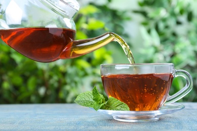 Photo of Pouring fresh mint tea into cup on blue wooden table, closeup