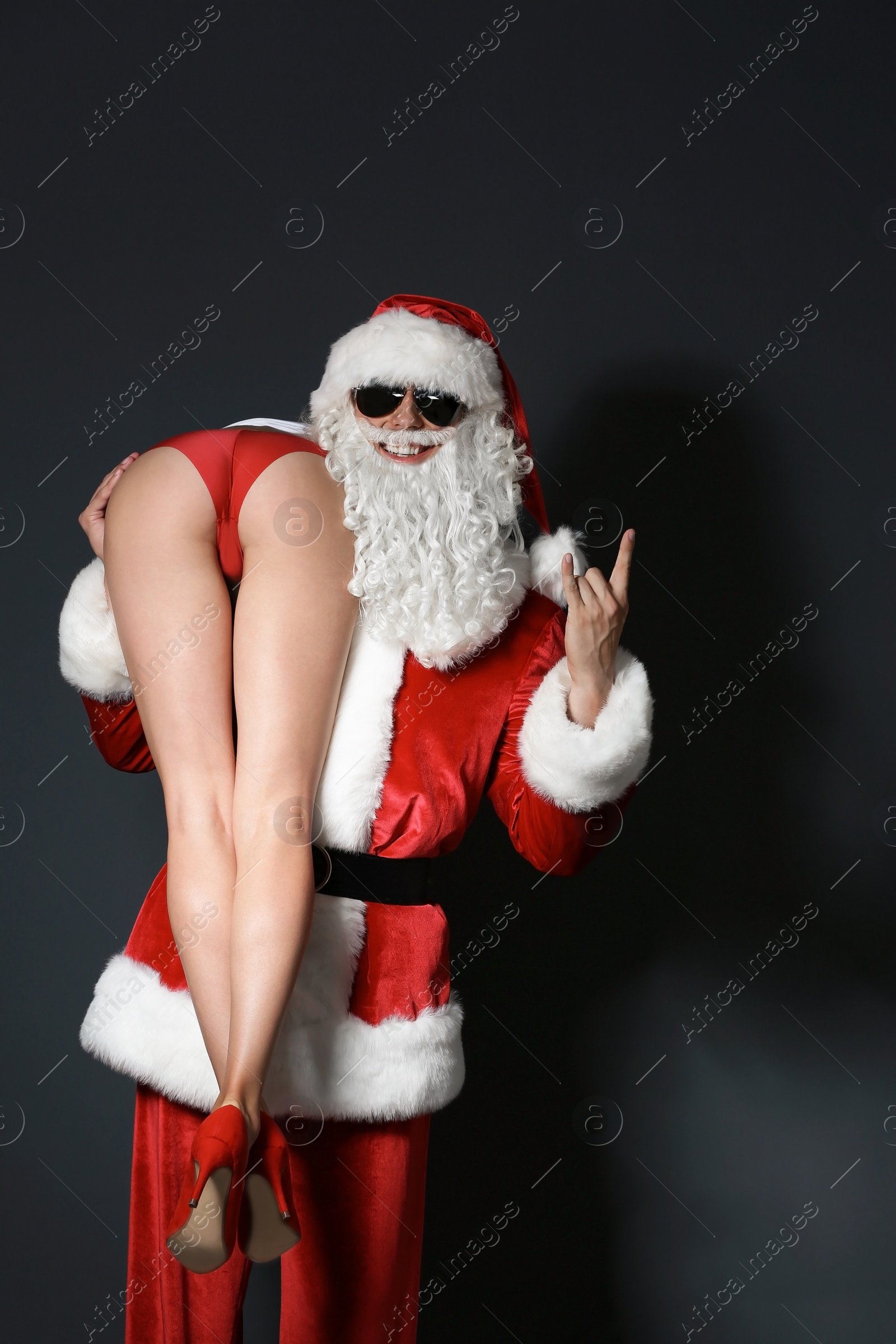 Photo of Young Santa Claus holding sexy naked woman on dark background
