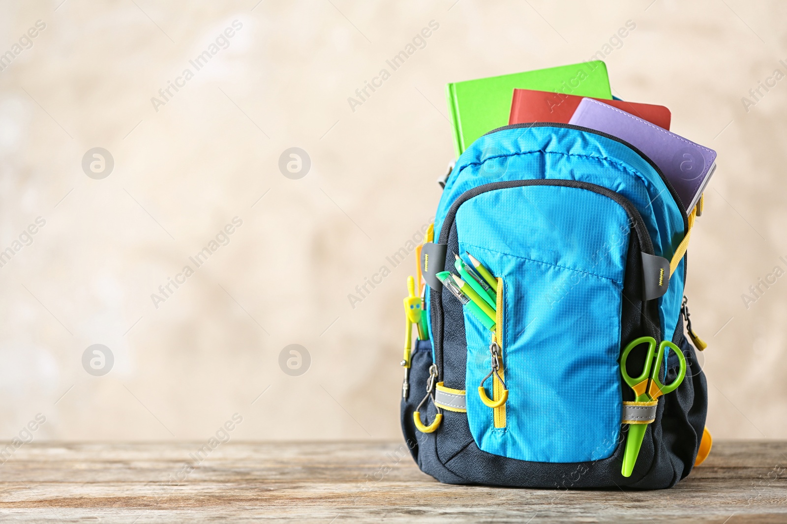 Photo of Backpack with school stationery on table against color background