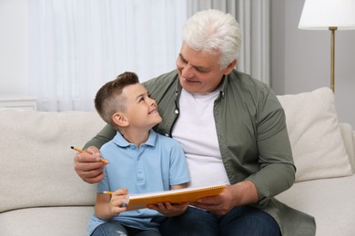 Little boy with his grandfather solving sudoku puzzle on sofa at home