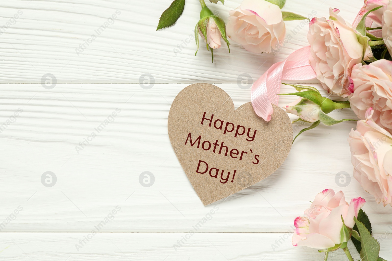 Image of Happy Mother's Day. Heart shaped greeting label and beautiful flowers on white wooden table